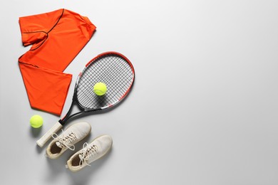 Photo of Tennis racket, balls, sneakers and orange shirt on grey background, flat lay. Space for text