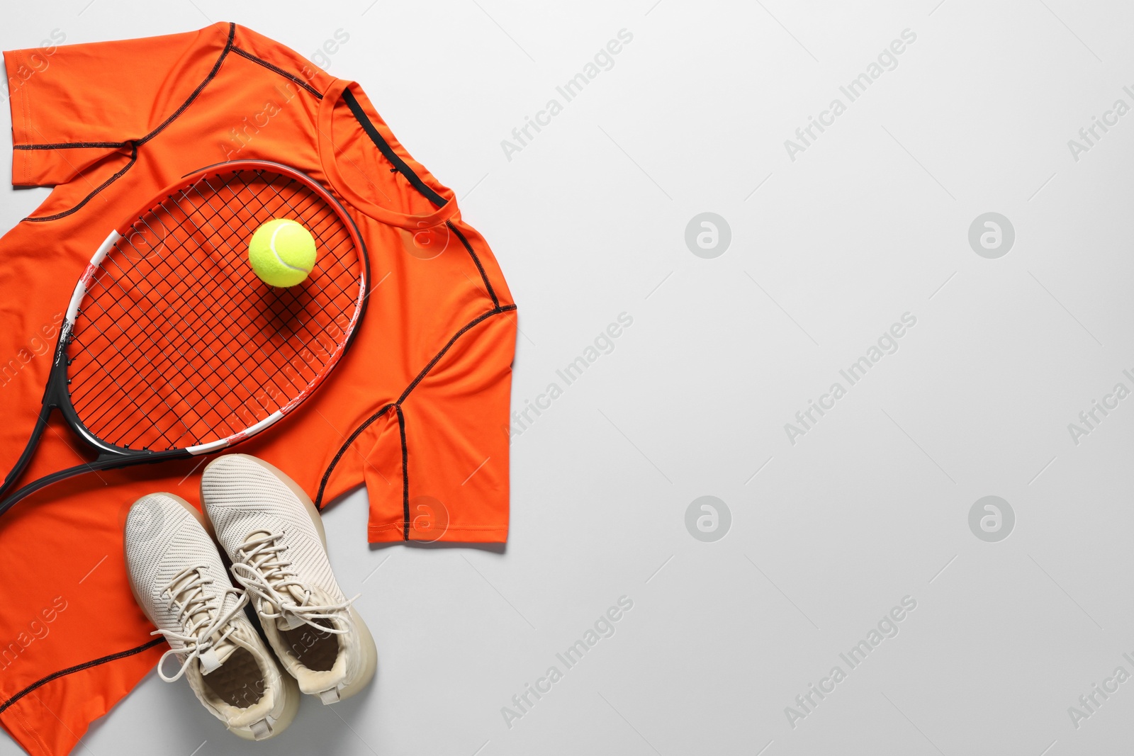 Photo of Tennis racket, ball, sneakers and orange shirt on grey background, flat lay. Space for text