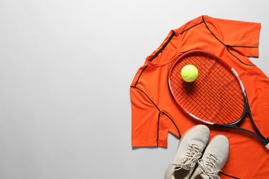 Photo of Tennis racket, ball, sneakers and orange shirt on grey background, flat lay. Space for text