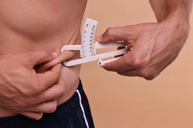 Photo of Man measuring body fat with caliper on beige background, closeup