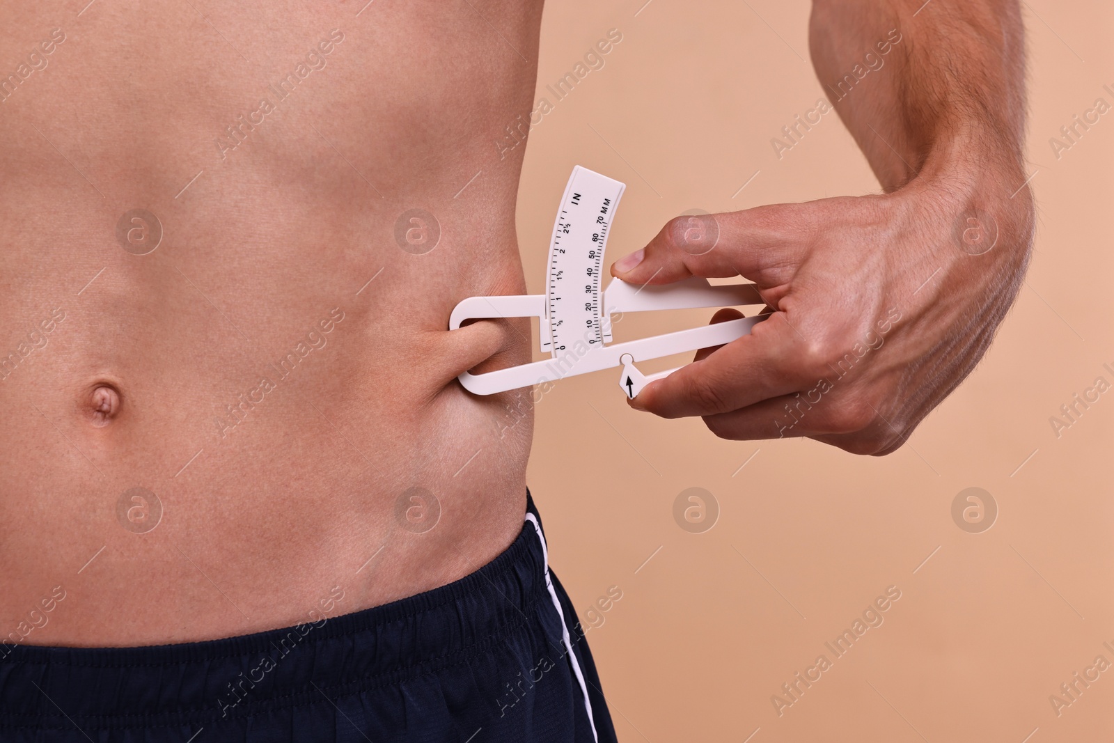 Photo of Man measuring body fat with caliper on beige background, closeup