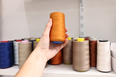 Photo of Woman holding spool of thread near shelf in professional workshop, closeup