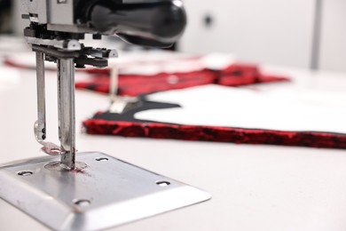 Photo of Machine and fabric on white table in professional workshop, closeup