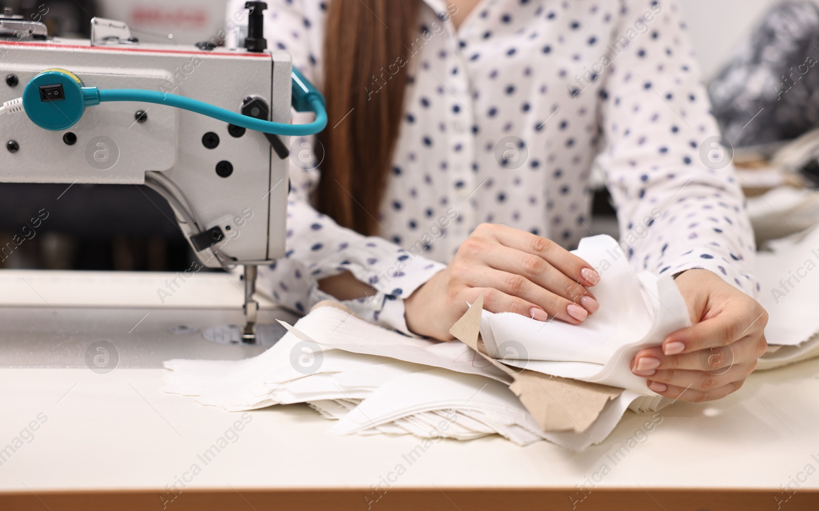 Photo of Young woman with sewing machine working at white table in professional workshop, closeup