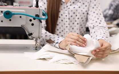 Photo of Young woman with sewing machine working at white table in professional workshop, closeup