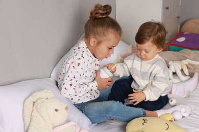 Photo of Sister and brother playing with toy pyramid on bed indoors