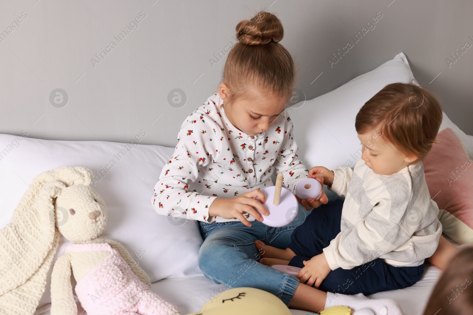 Photo of Sister and brother playing with toy pyramid on bed indoors