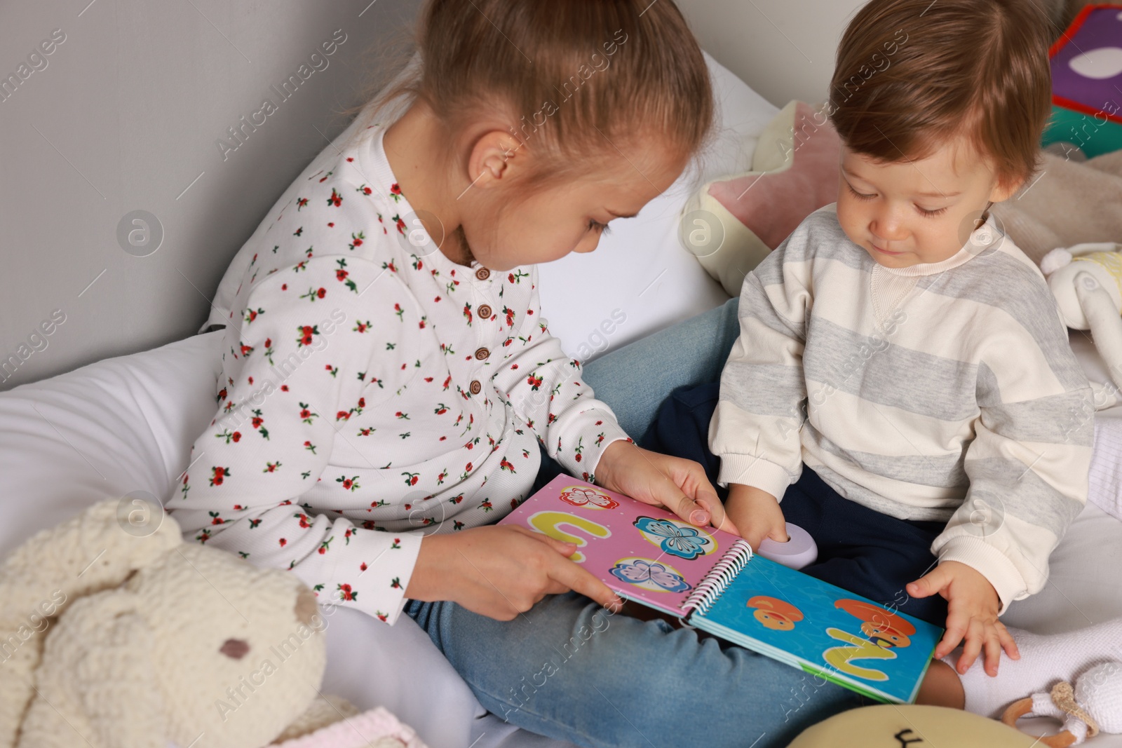 Photo of Sister and brother reading book together on bed indoors