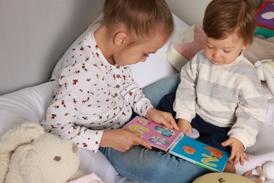 Photo of Sister and brother reading book together on bed indoors