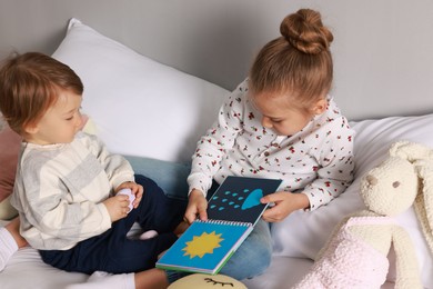 Photo of Sister and brother reading book together on bed indoors