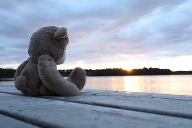 Lonely teddy bear on deck near river, space for text