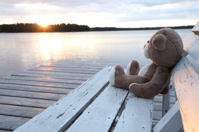 Photo of Lonely teddy bear on bench near river