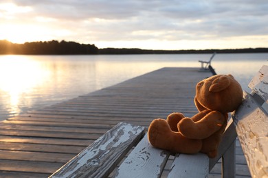 Lonely teddy bear on bench near river