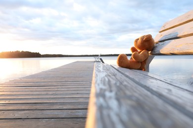 Lonely teddy bear on bench near river