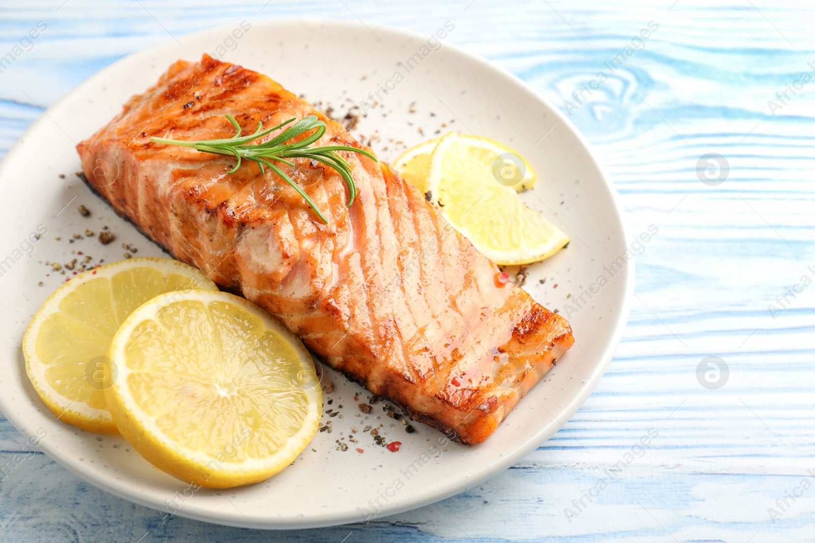 Photo of Delicious grilled salmon fillet served on light blue wooden table, closeup