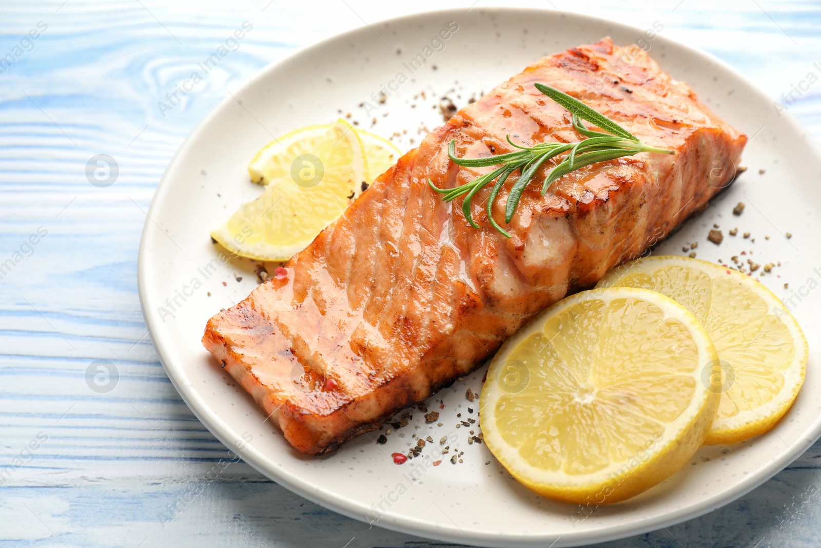 Photo of Delicious grilled salmon fillet served on light blue wooden table, closeup