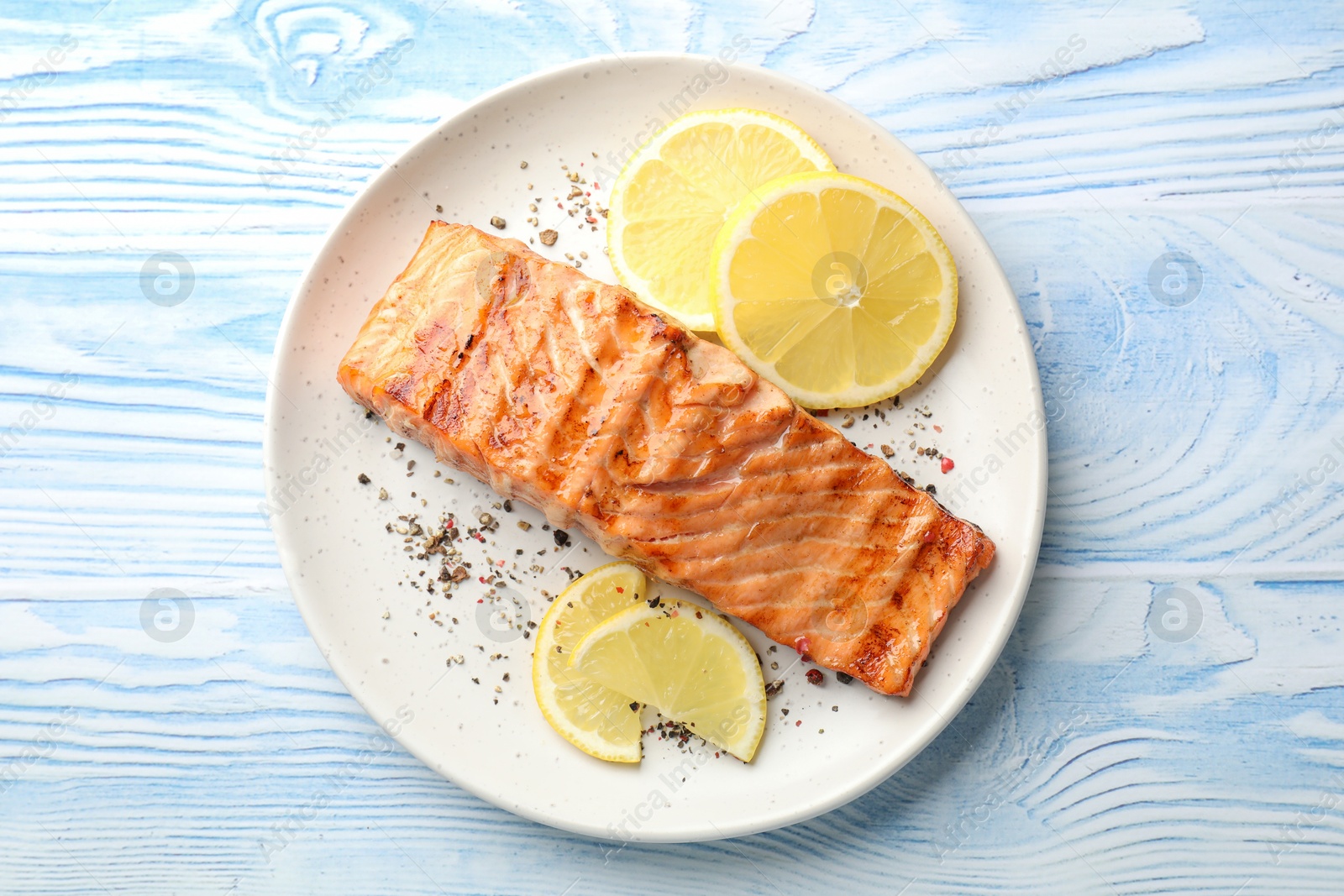 Photo of Delicious grilled salmon fillet served on light blue wooden table, top view