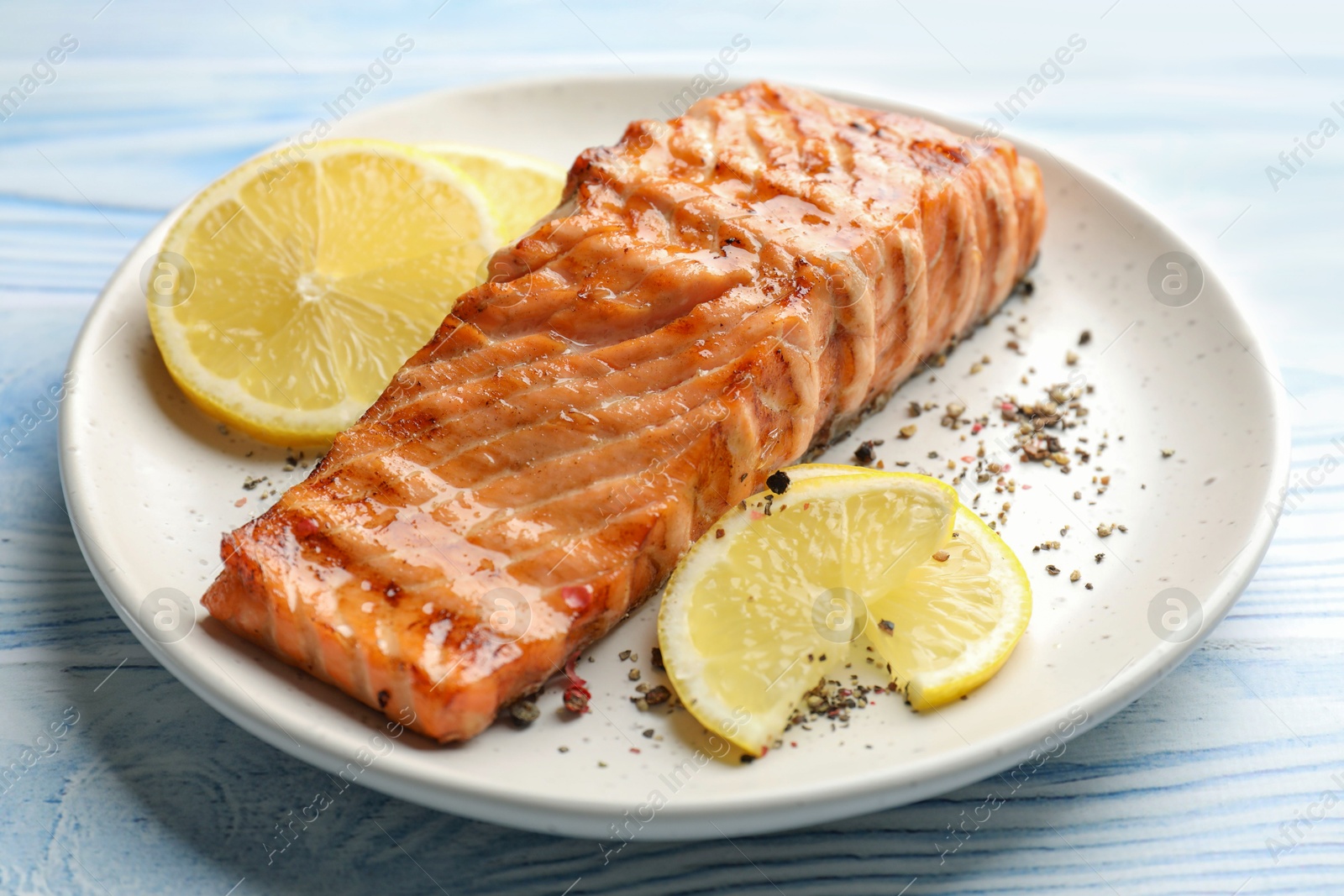 Photo of Delicious grilled salmon fillet served on light blue wooden table, closeup