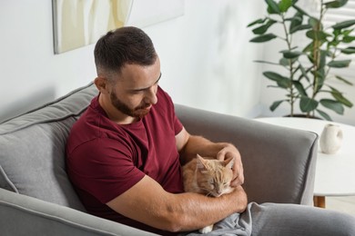 Man petting cute ginger cat on armchair at home