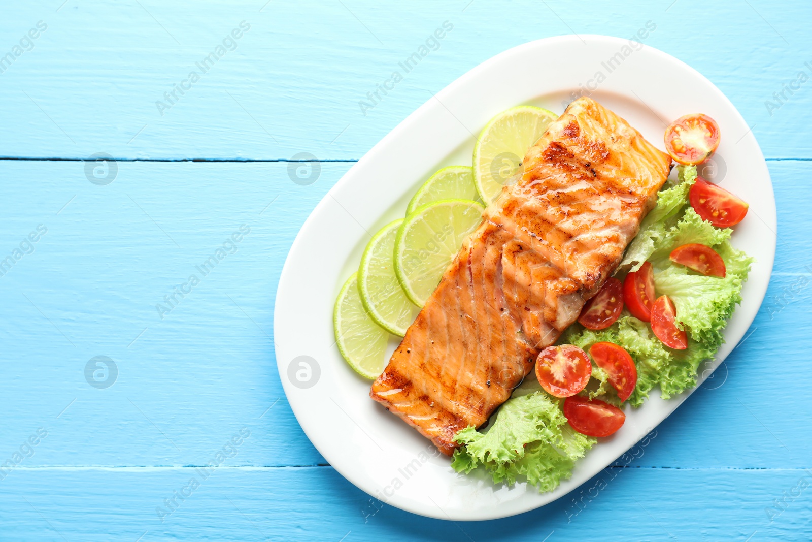 Photo of Delicious grilled salmon fillet with vegetable salad and lime on light blue wooden table, top view. Space for text