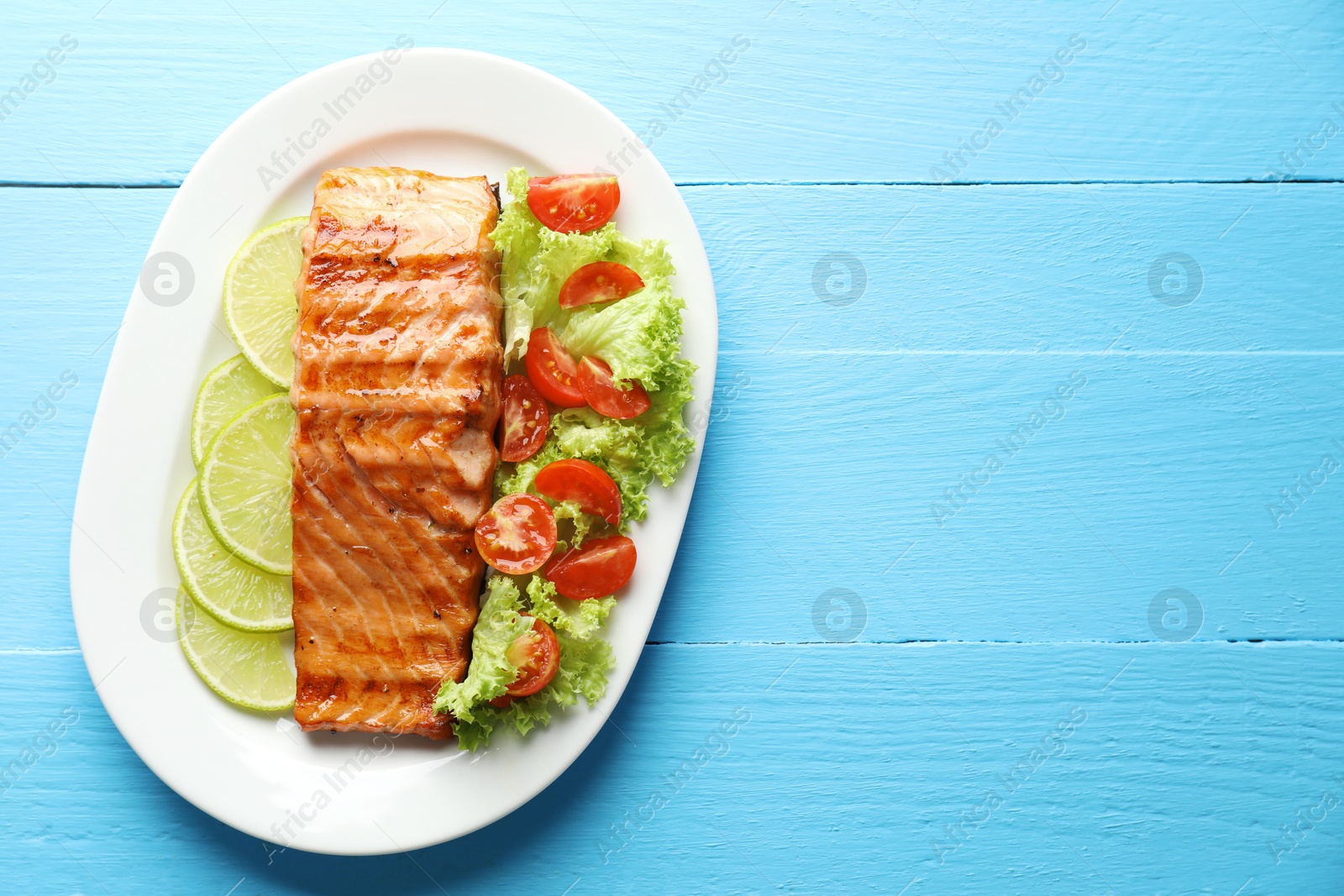 Photo of Delicious grilled salmon fillet with vegetable salad and lime on light blue wooden table, top view. Space for text