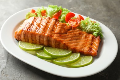 Photo of Delicious grilled salmon fillet with vegetable salad and lime on grey textured table, closeup