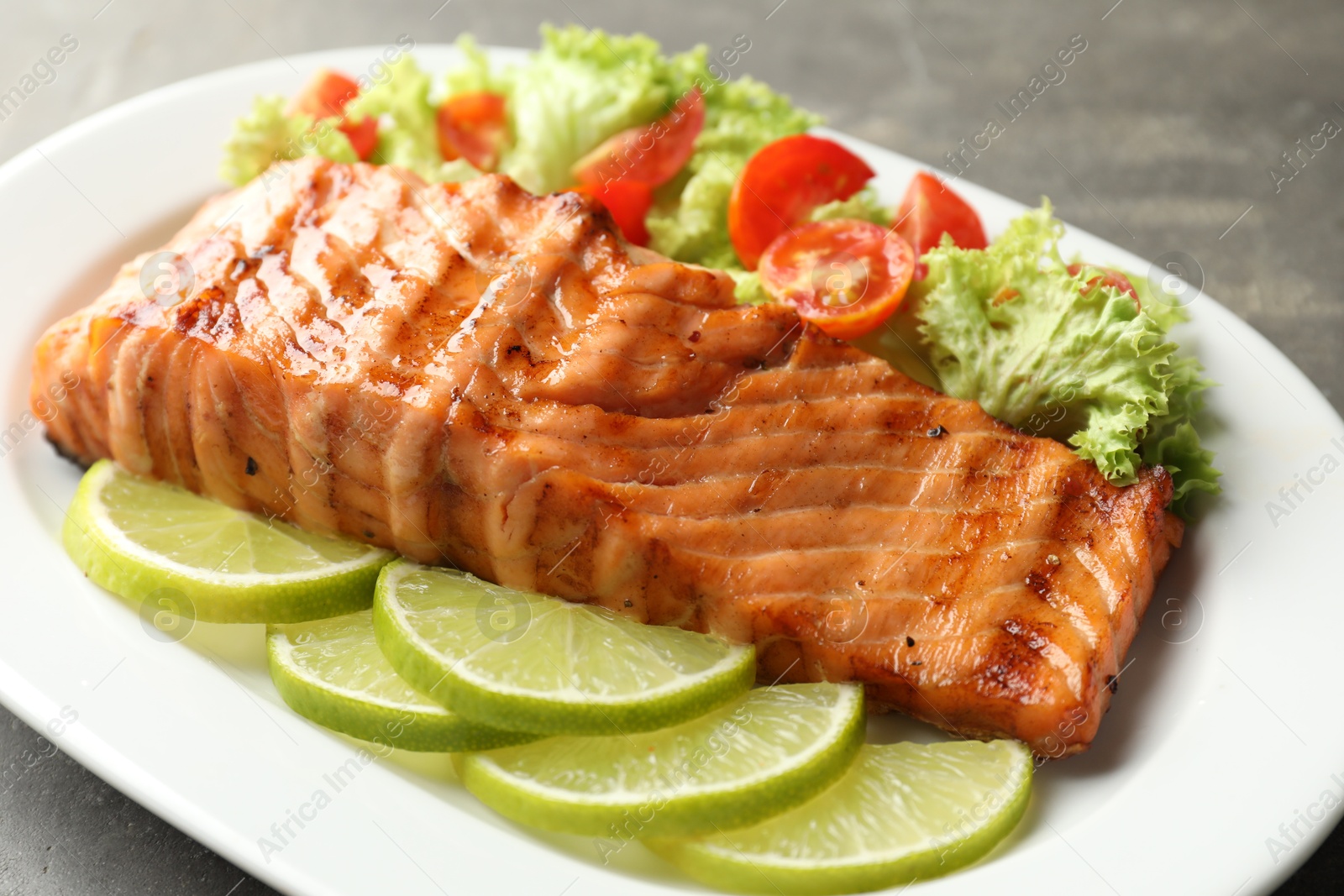 Photo of Delicious grilled salmon fillet with vegetable salad and lime on grey table, closeup