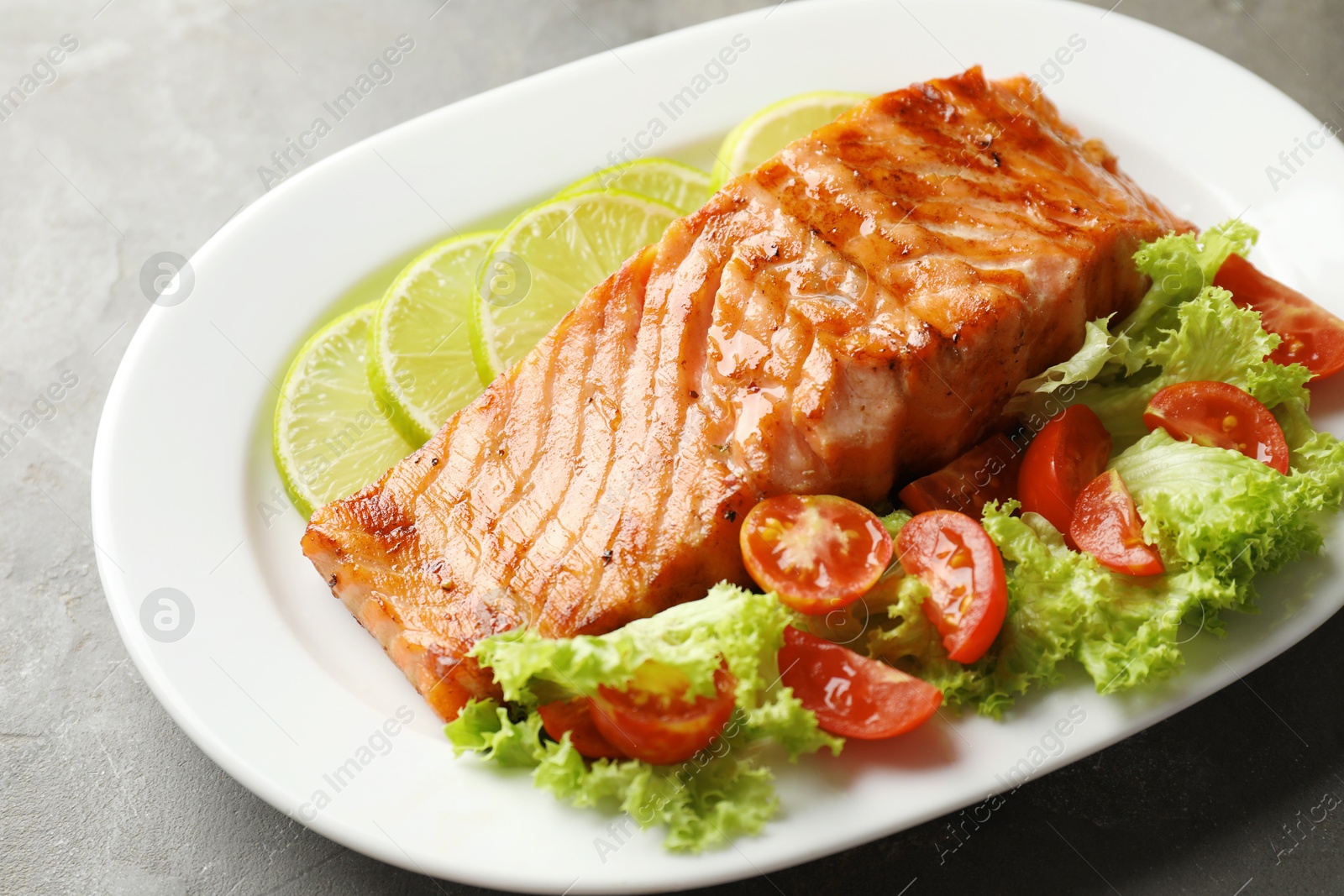 Photo of Delicious grilled salmon fillet with vegetable salad and lime on grey table, closeup