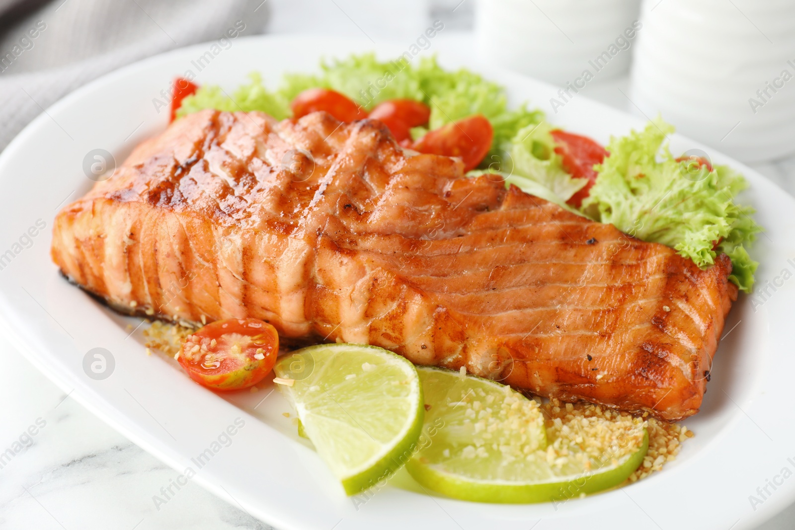 Photo of Delicious grilled salmon fillet with vegetable salad and lime on white marble table, closeup