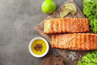 Photo of Delicious grilled salmon fillets served on grey textured table, flat lay. Space for text