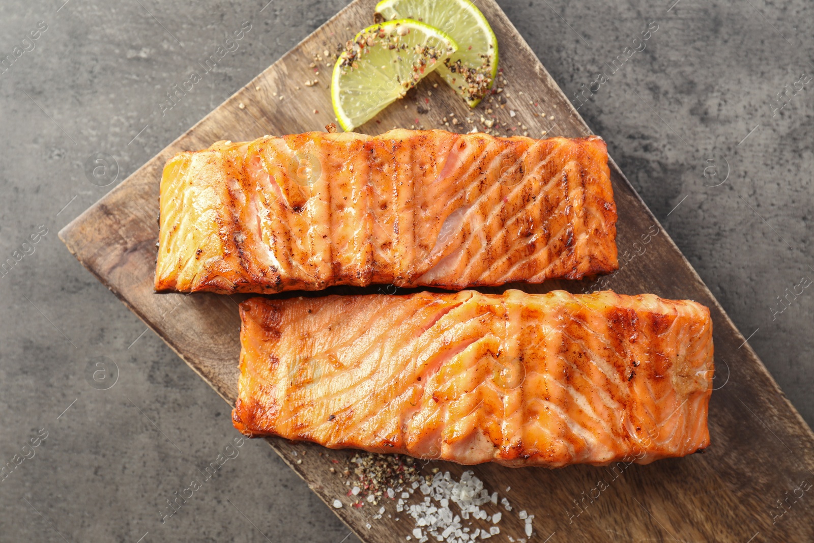 Photo of Delicious grilled salmon fillets served on grey textured table, flat lay