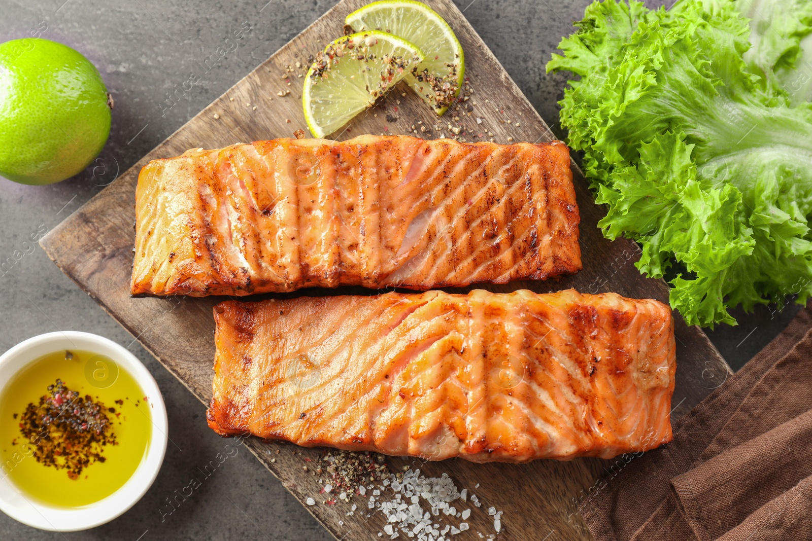 Photo of Delicious grilled salmon fillets served on grey textured table, flat lay