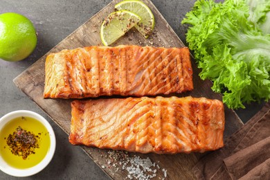 Photo of Delicious grilled salmon fillets served on grey textured table, flat lay