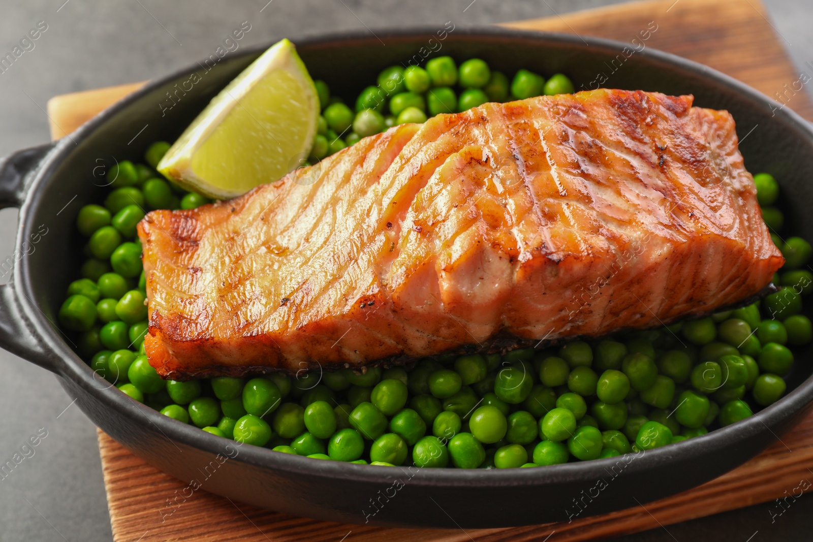 Photo of Delicious grilled salmon fillet with green peas and lime in baking dish on grey table, closeup