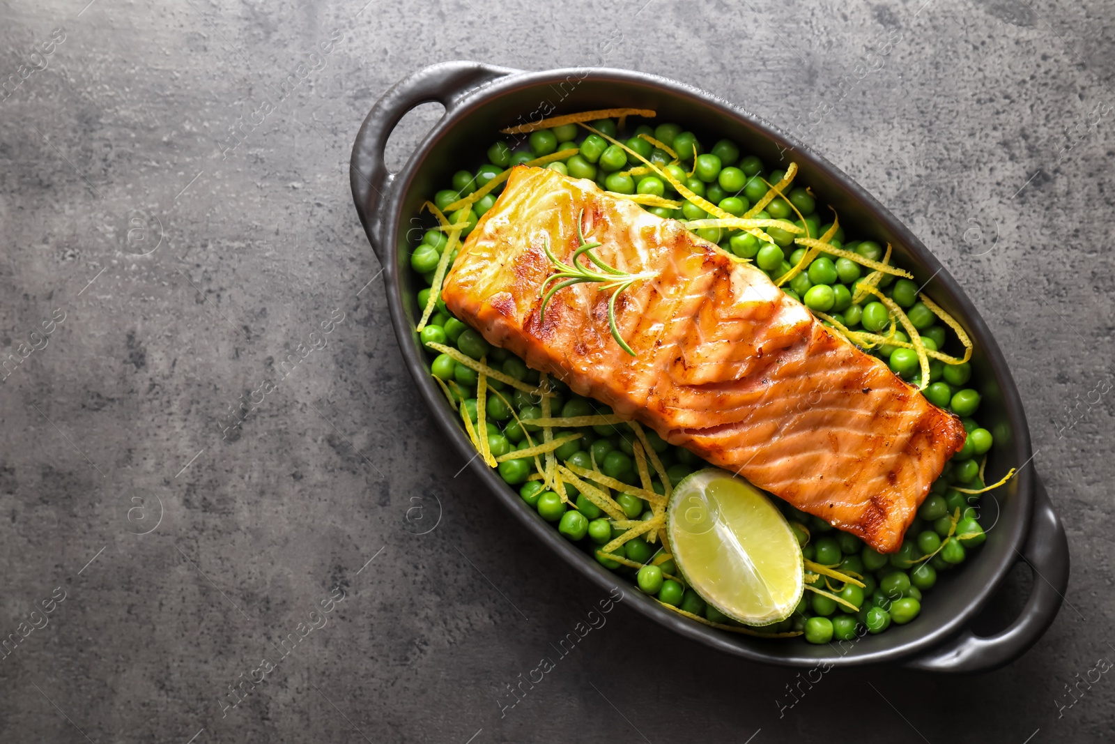 Photo of Delicious grilled salmon fillet with green peas and lime in baking dish on grey textured table, top view. Space for text