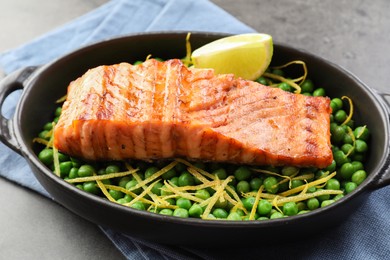 Photo of Delicious grilled salmon fillet with green peas and lime in baking dish on grey table, closeup