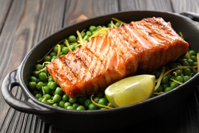 Photo of Delicious grilled salmon fillet with green peas and lime in baking dish on wooden table, closeup