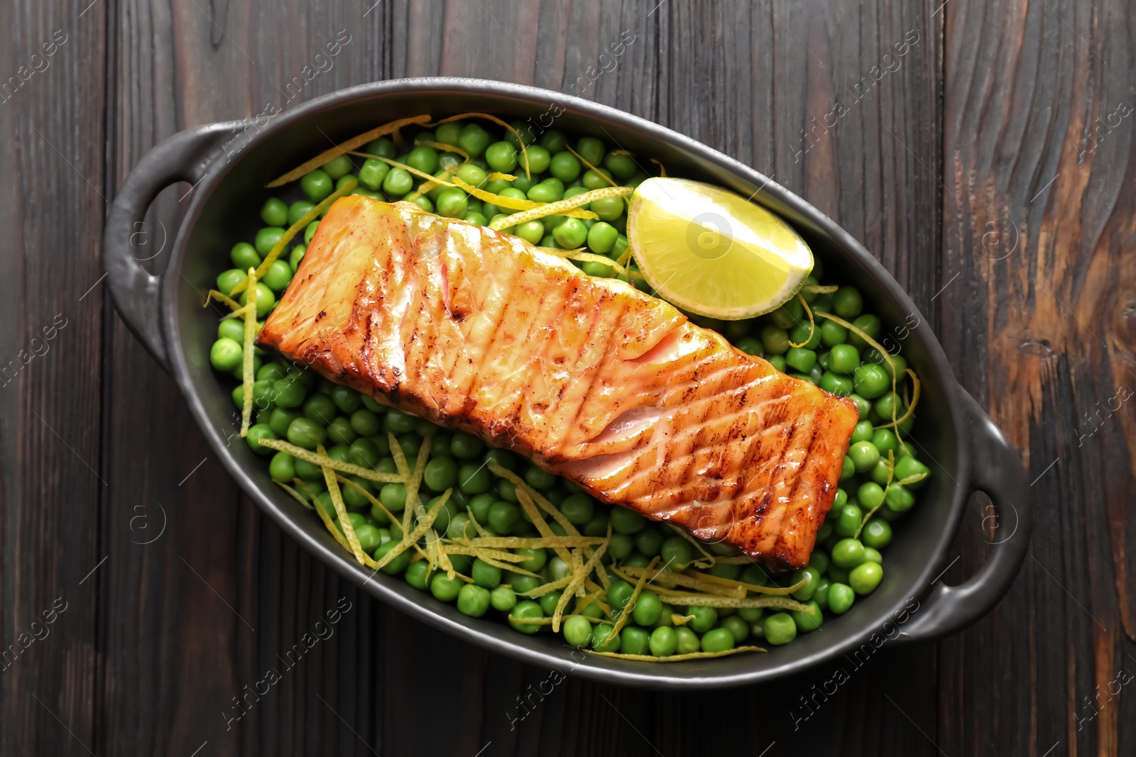 Photo of Delicious grilled salmon fillet with green peas and lime in baking dish on wooden table, top view