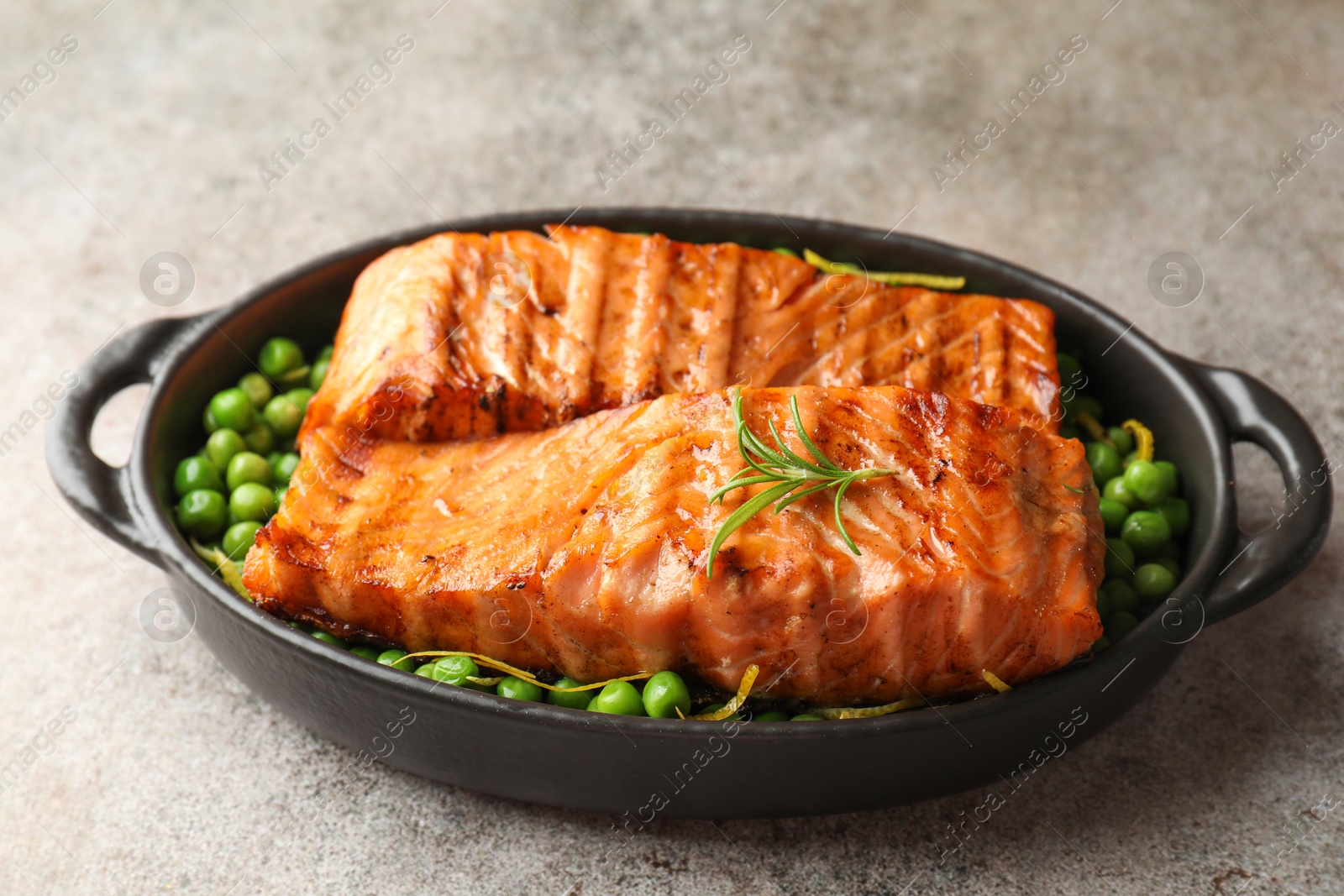 Photo of Delicious grilled salmon fillets with rosemary and green peas in baking dish on grey textured table, closeup