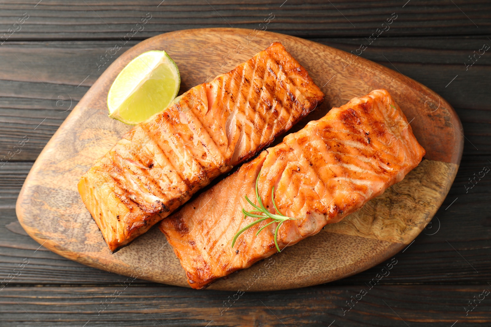 Photo of Delicious grilled salmon fillets with lime and rosemary on wooden table, top view