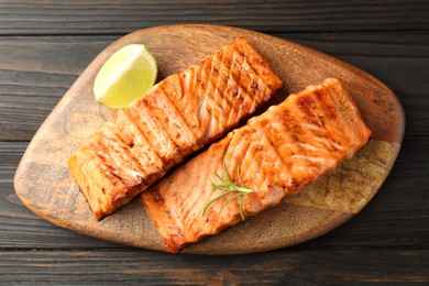 Photo of Delicious grilled salmon fillets with lime and rosemary on wooden table, top view