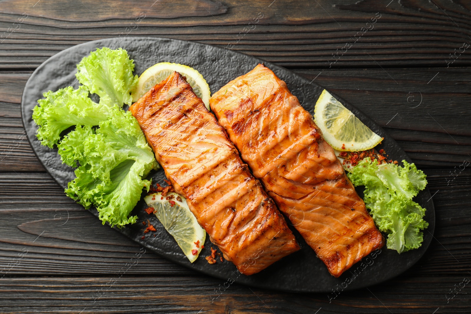 Photo of Delicious grilled salmon fillets with lettuce and lemon on wooden table, top view