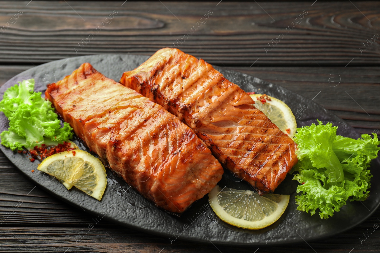 Photo of Delicious grilled salmon fillets with lettuce and lemon on wooden table, closeup