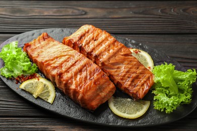 Photo of Delicious grilled salmon fillets with lettuce and lemon on wooden table, closeup