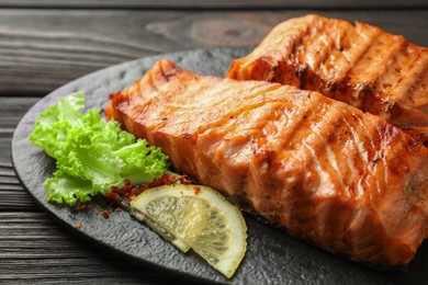 Photo of Delicious grilled salmon fillets with lettuce and lemon on wooden table, closeup