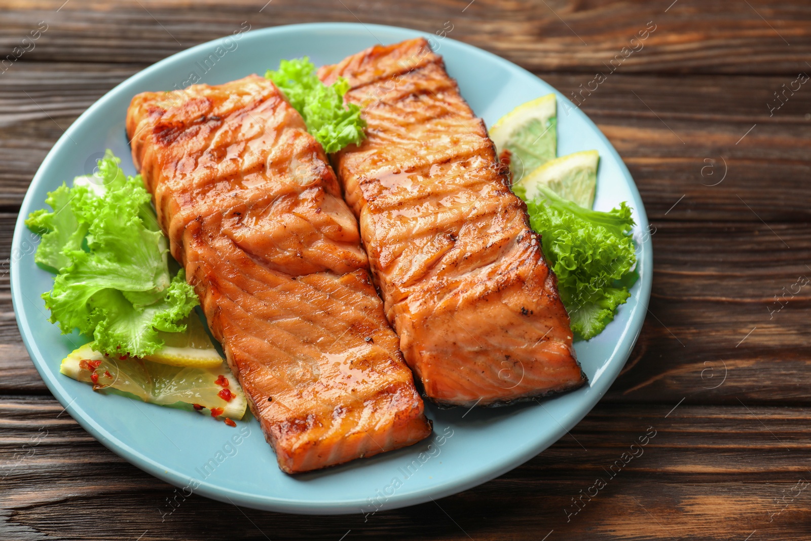 Photo of Delicious grilled salmon fillets with lettuce and lemon on wooden table, closeup