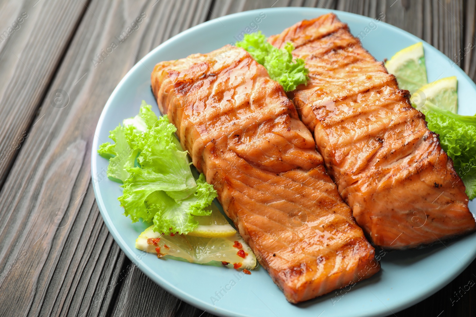 Photo of Delicious grilled salmon fillets with lettuce and lemon on wooden table, closeup