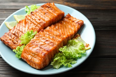 Photo of Delicious grilled salmon fillets with lettuce and lemon on wooden table, closeup