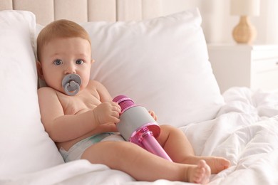 Photo of Cute little baby with microphone and pacifier on bed at home, space for text