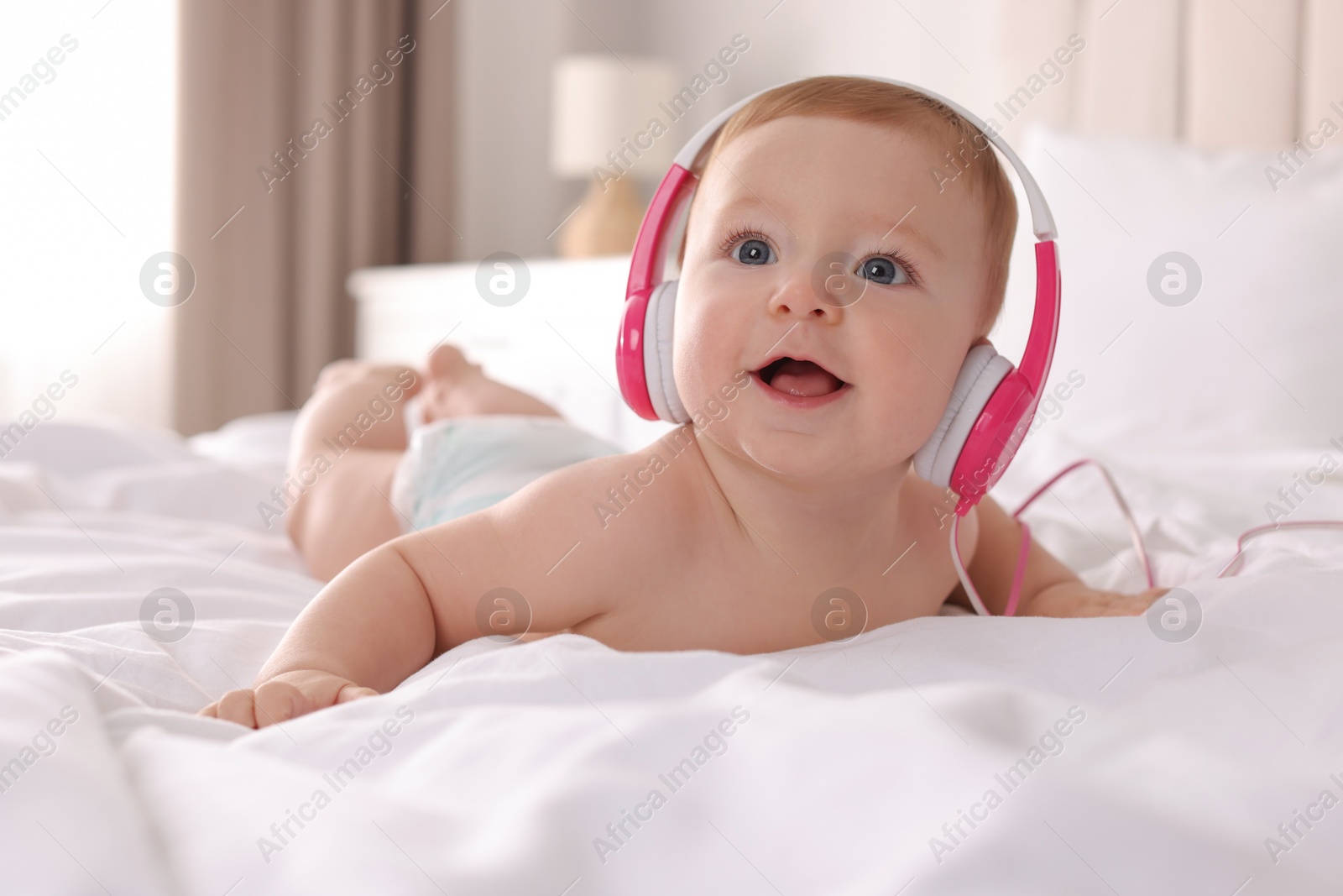 Photo of Cute little baby with headphones on bed at home